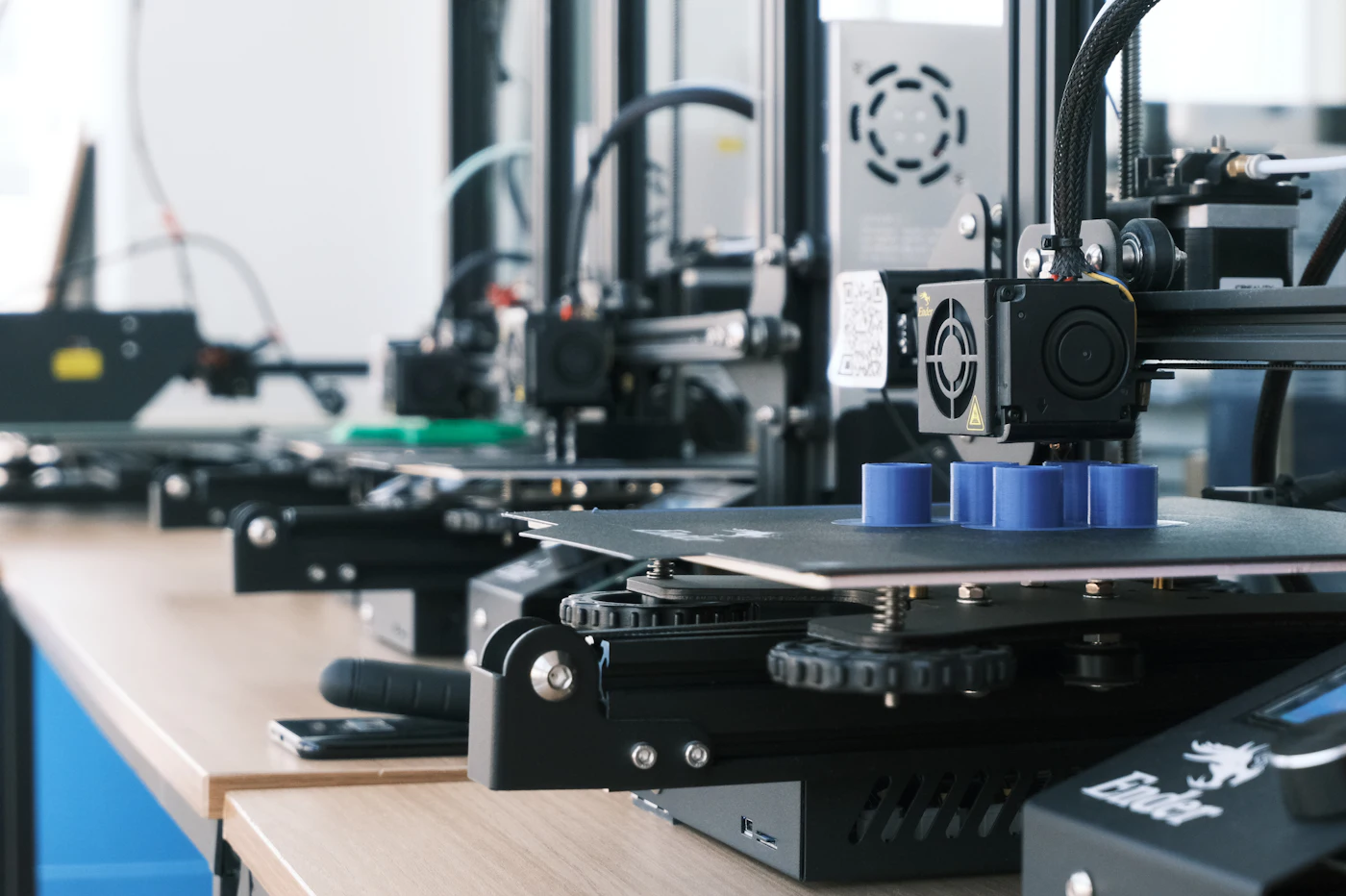 Row of 3D printers producing blue plastic parts layer by layer in a workshop