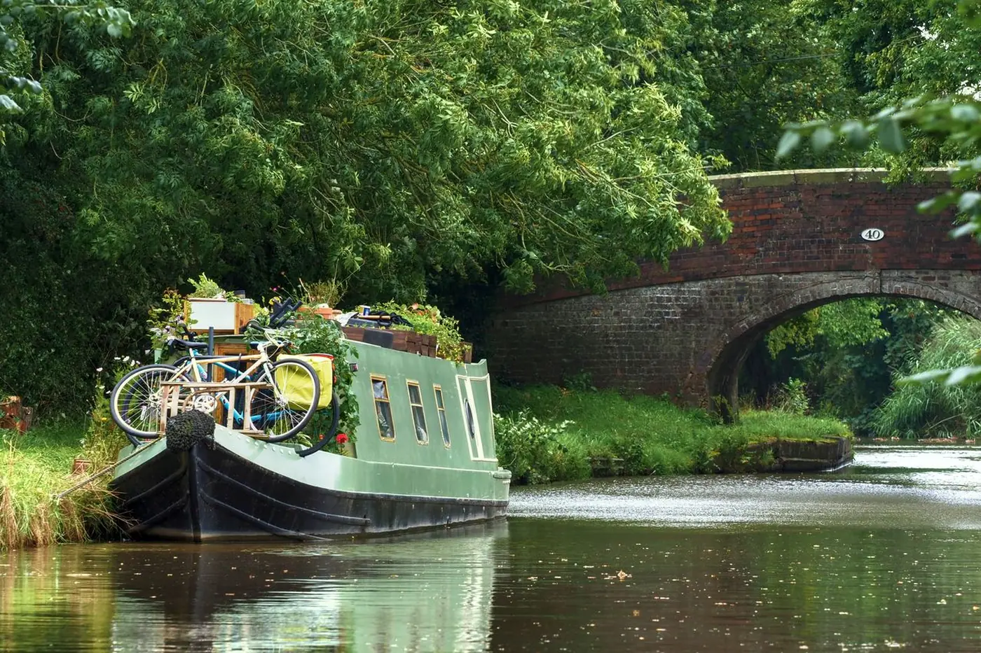 Narrowboat moored by a brick bridge on a leafy canal
