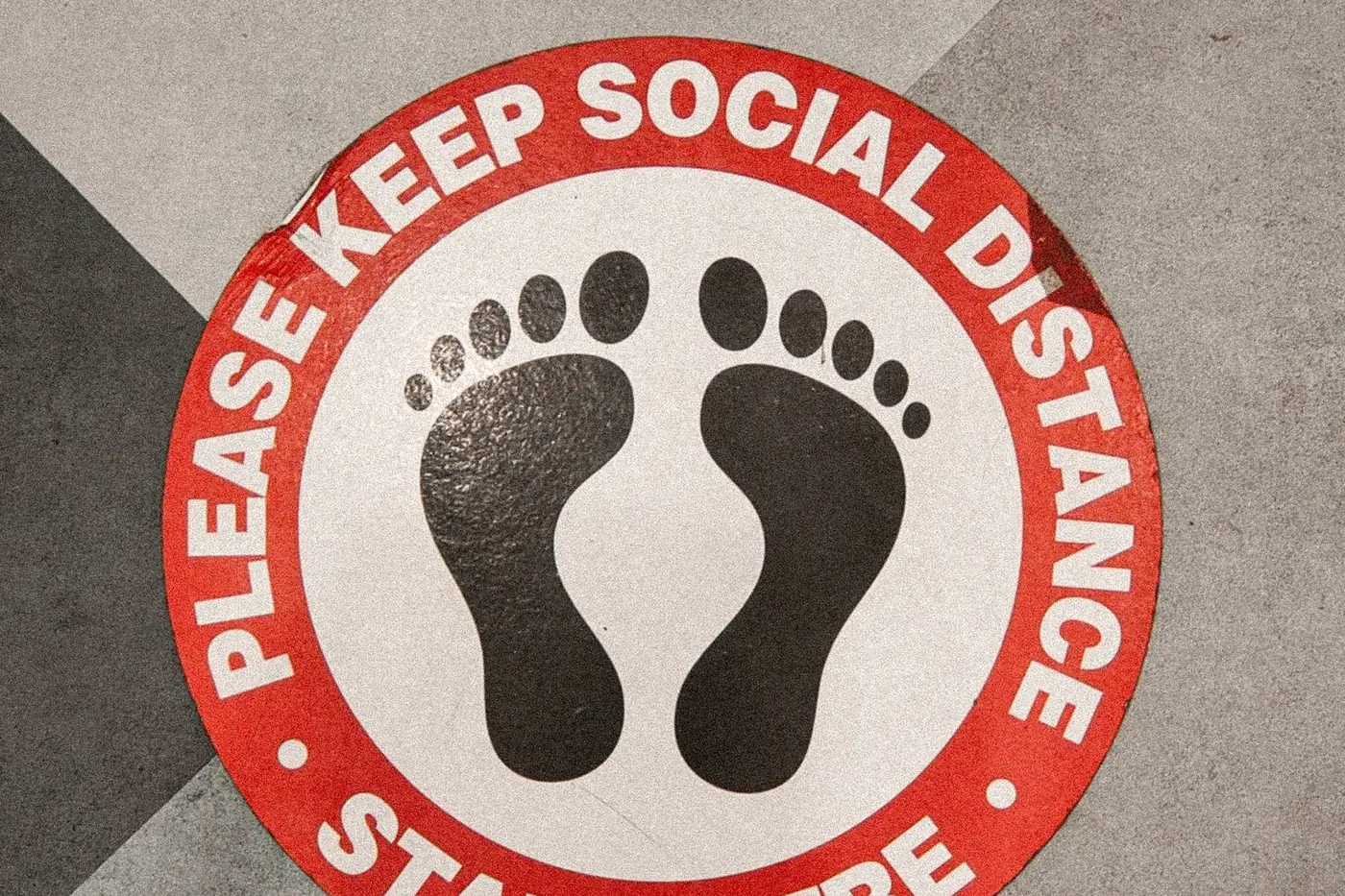 Round printed floor sign with footprints reading stand here