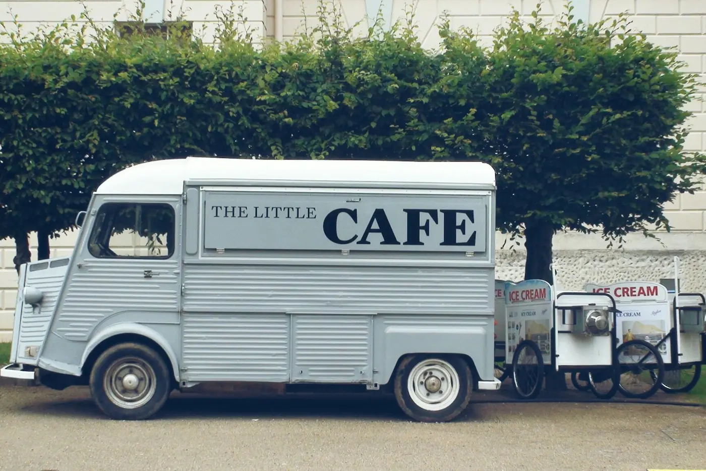 Grey vintage Citroën H van lettered The Little Cafe, parked beside two ice cream tricycles