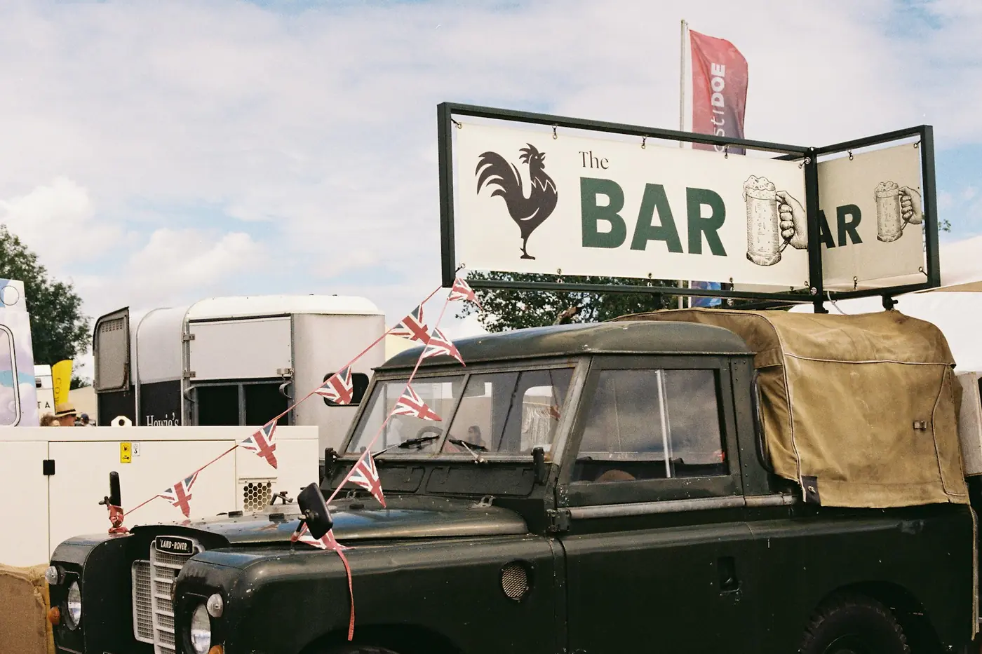 Classic Land Rover bar with a large signboard on the roof and Union Jack bunting, horsebox trailers behind