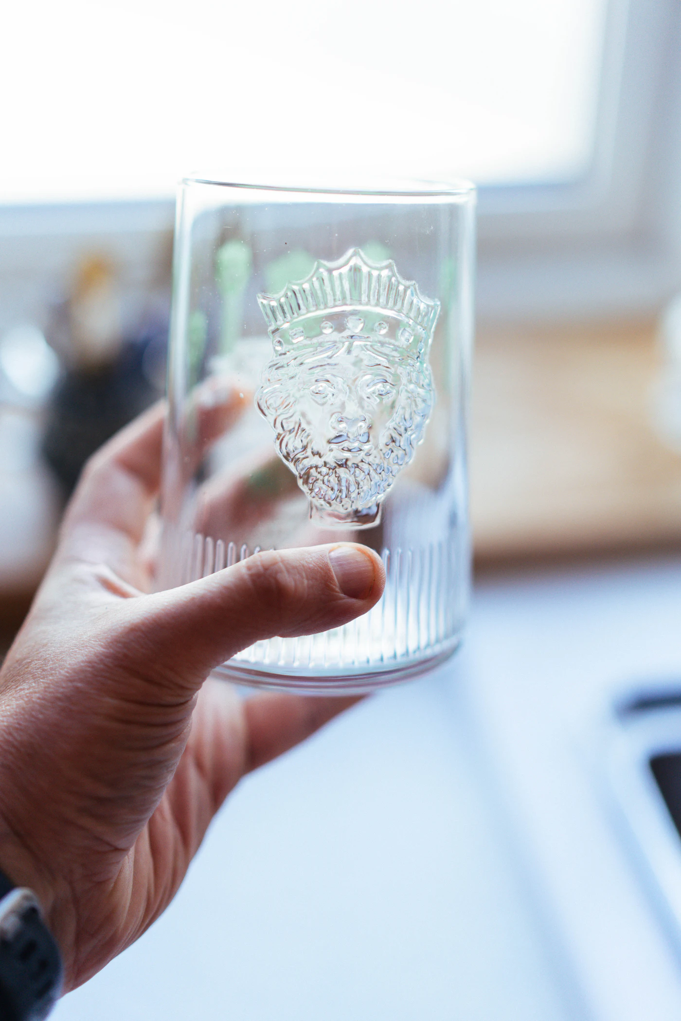 Hand holding a whisky tumbler etched with a detailed heraldic crest design