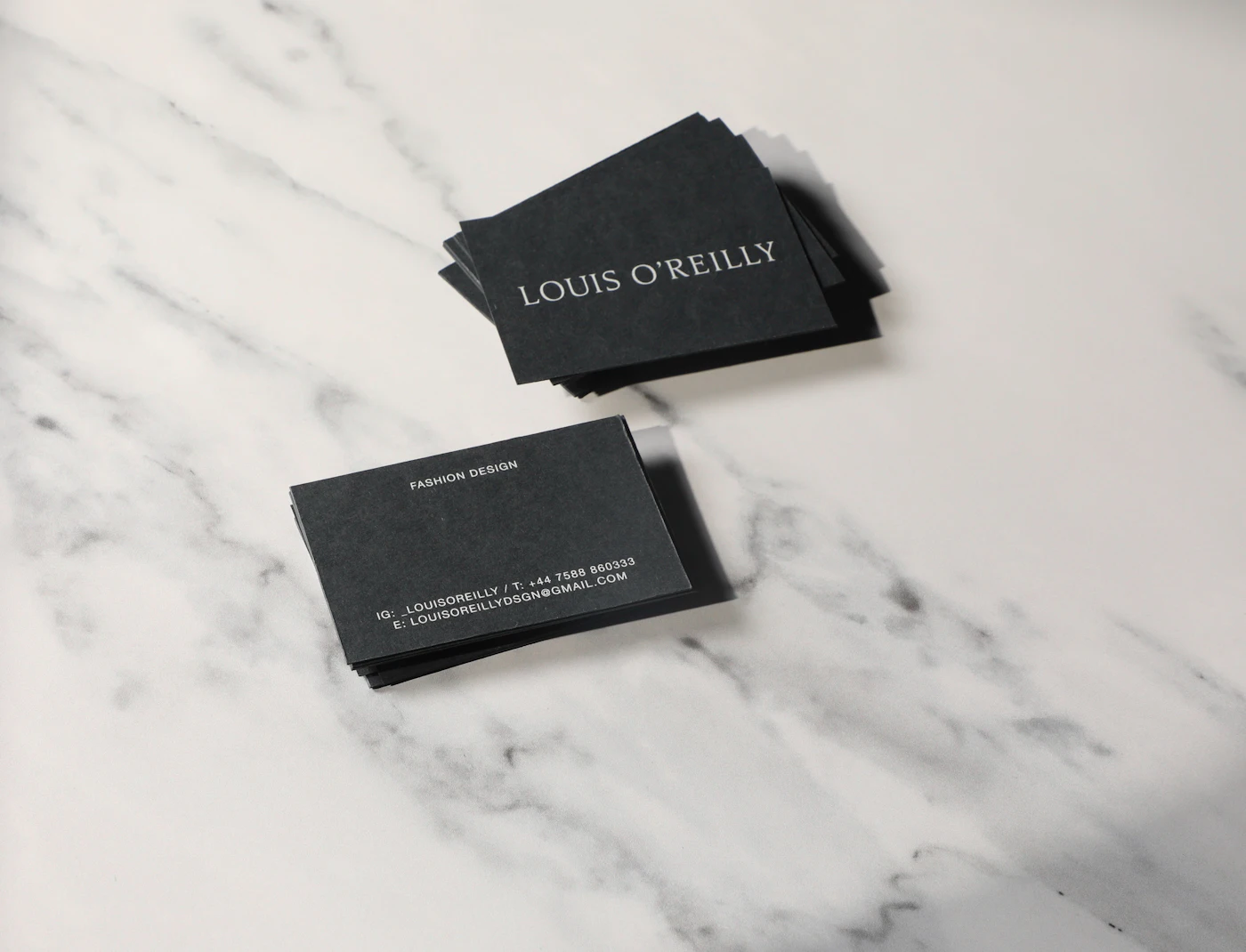Pair of printed black business cards resting on a white marble counter top