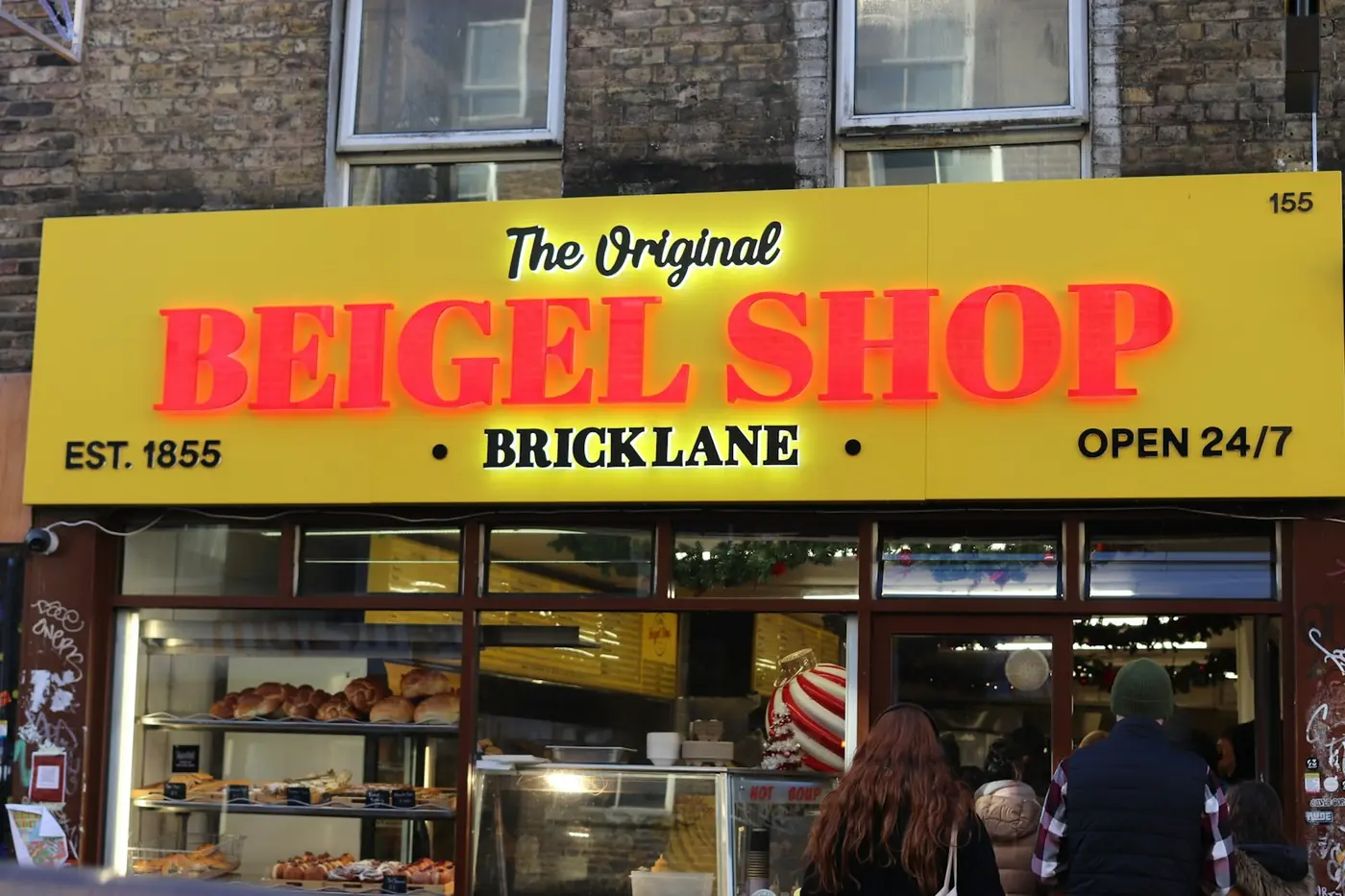 Illuminated yellow fascia sign for The Original Beigel Shop on Brick Lane with red lit lettering