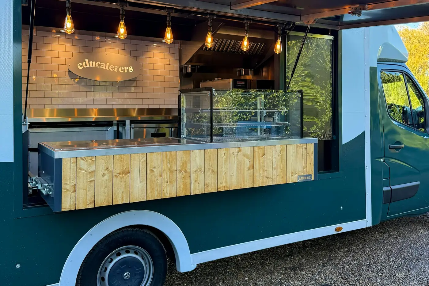 Dark green catering van with its serving hatch open, a timber-clad counter and the business name lettered on the back wall