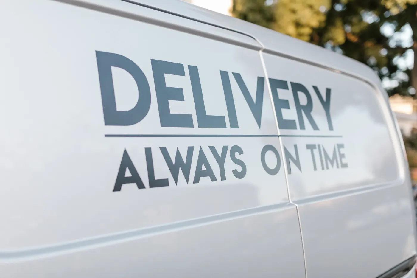Close-up of grey vinyl lettering reading Delivery Always On Time on a white van side