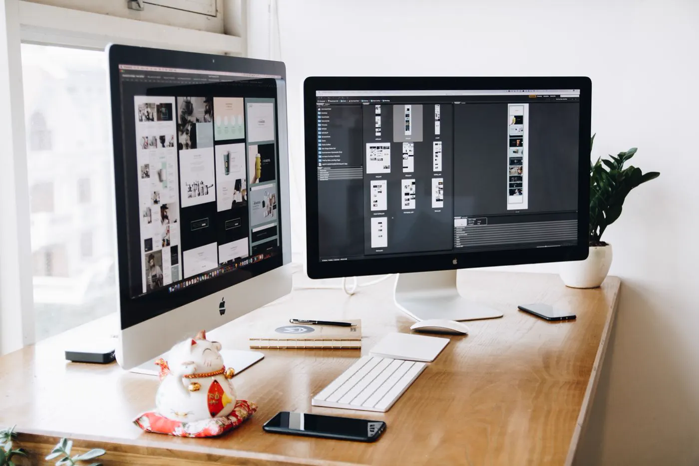 Designer's desk with two large monitors showing website layouts and image grids