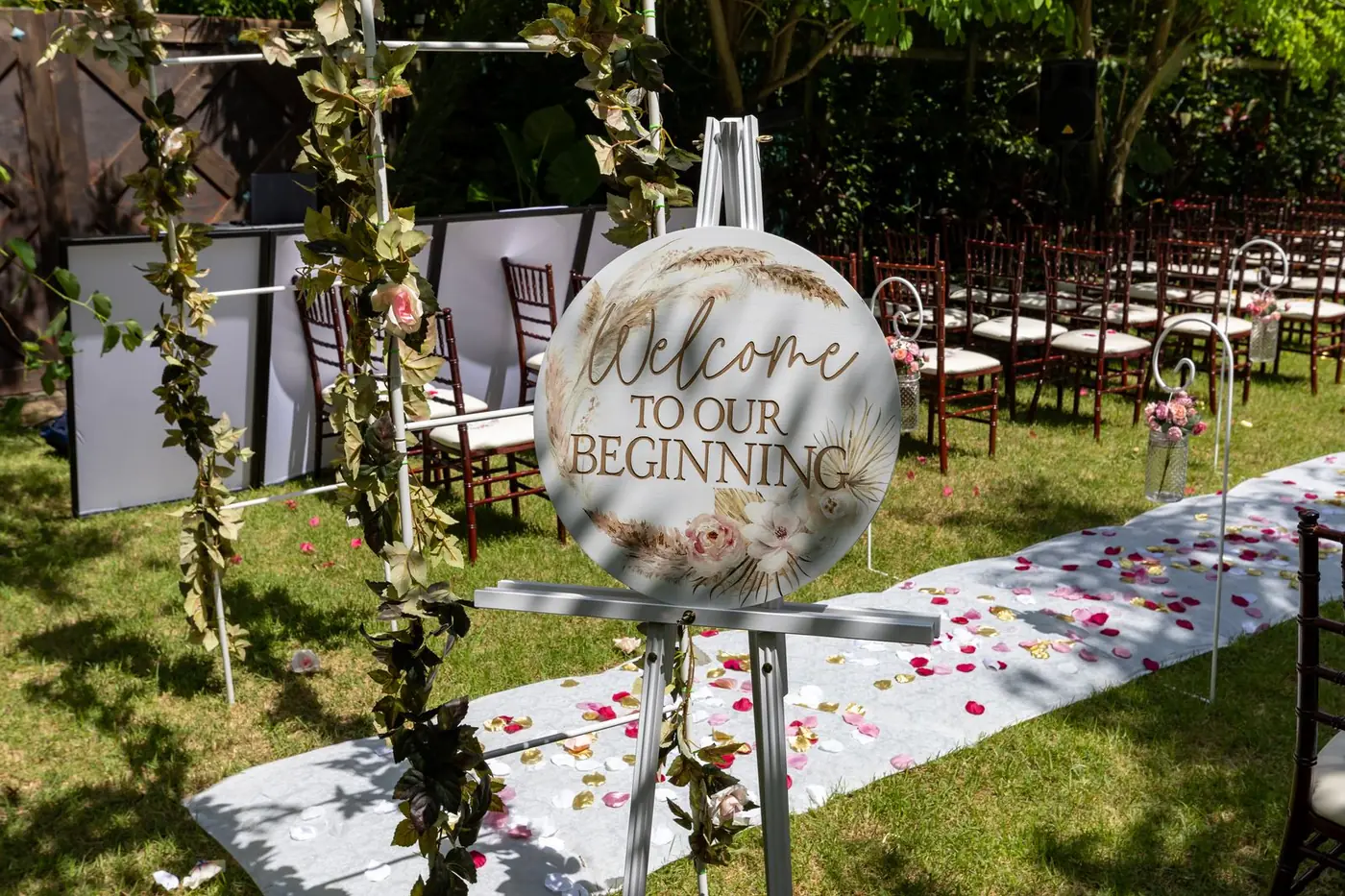 Round welcome sign on an easel at the end of an outdoor wedding aisle