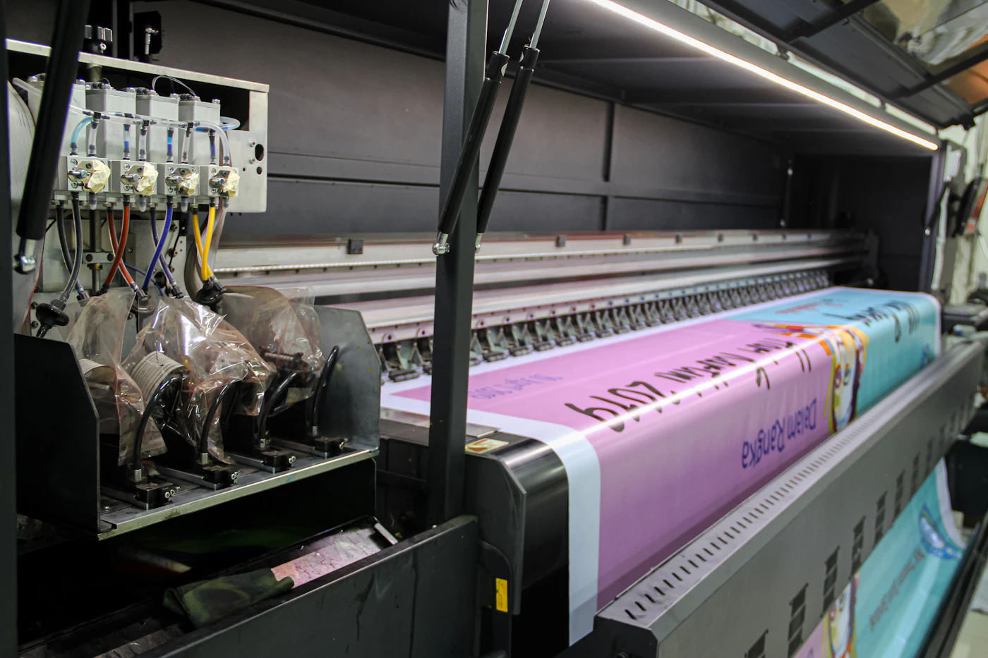 Wide format printer producing a bright pink vinyl banner in a print shop